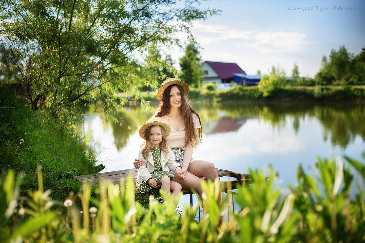 Мама и дочка обнимаются сидя у пруда - Дарья Дядькина