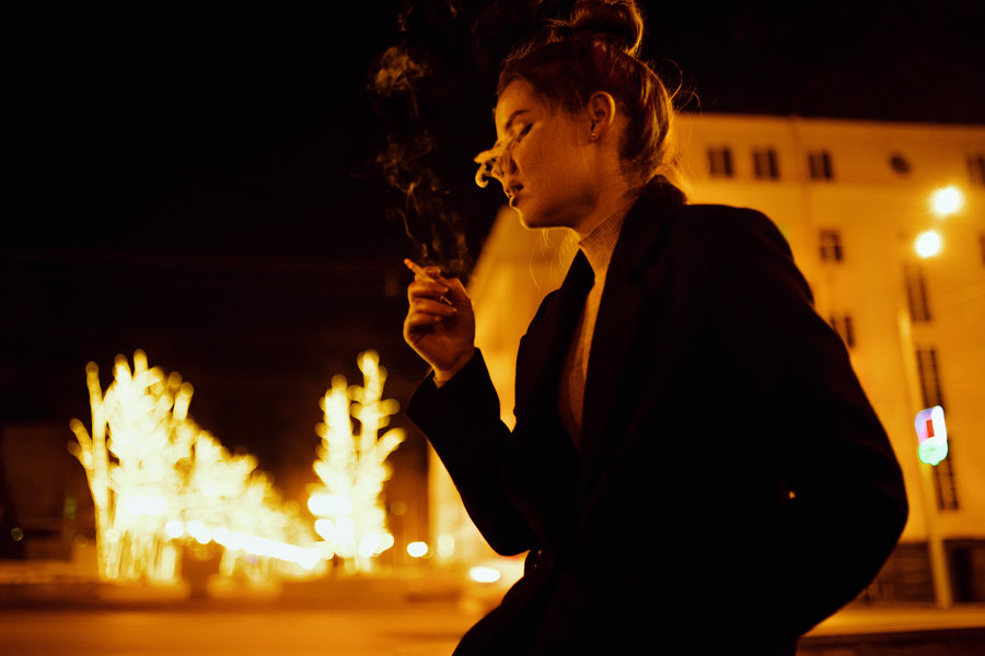 Девушка в пальто курит сигареты на фоне святящихся деревьев на улице в ночной Уфе - Lenar Abdrakhmanov