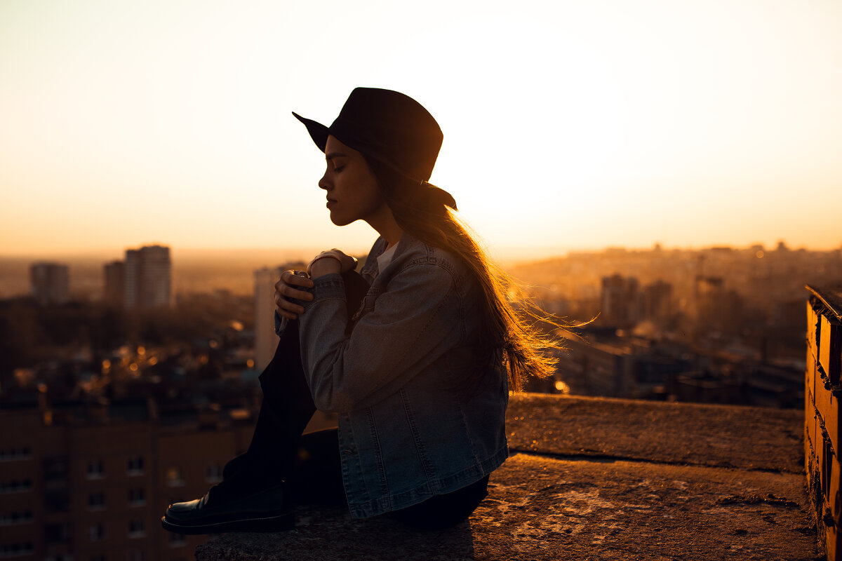 Девушка в шляпе и джинсовке сидит на крыше дома во время заката - Lenar Abdrakhmanov