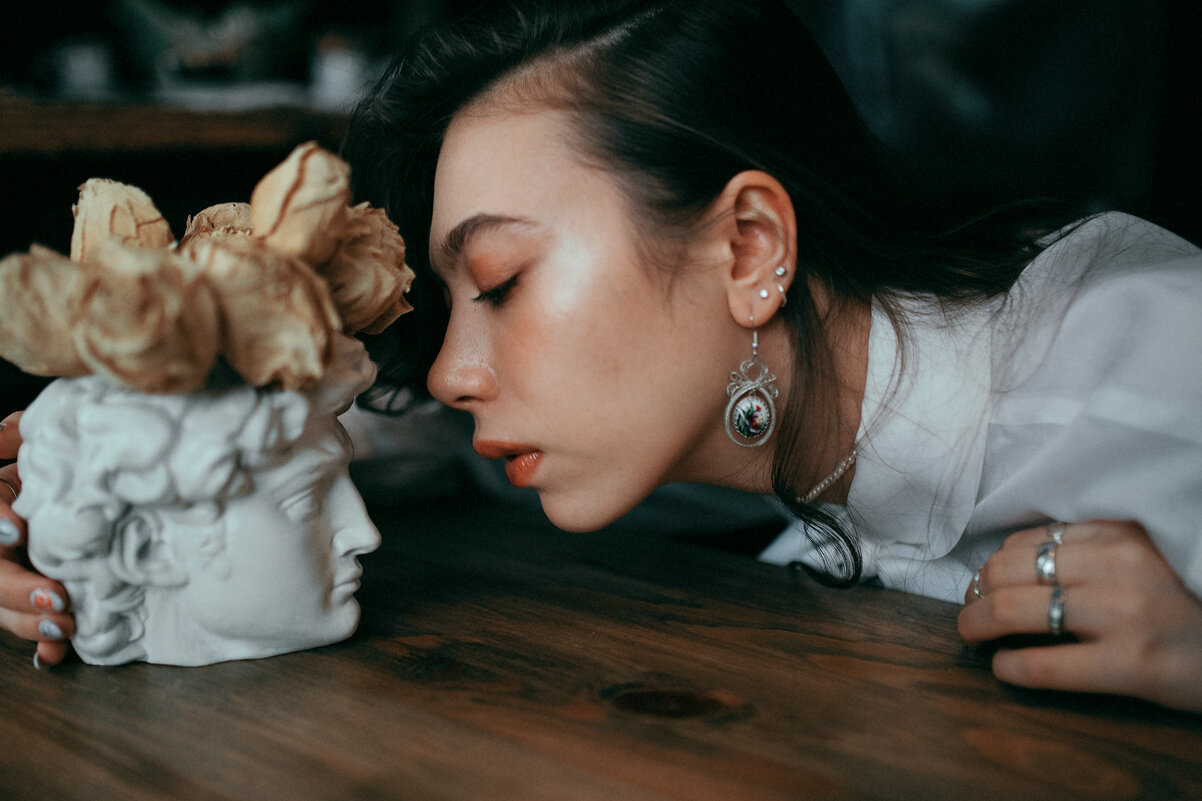 Девушка в белой рубашке с винтажными серьгами целует гипсовую голову с розами - Lenar Abdrakhmanov