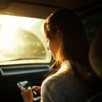Девушка держит телефон в руке сидя в машине на фоне солнечного блика во время заката :: Lenar Abdrakhmanov