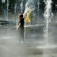 Малыш под струями воды и пара от фонтана.